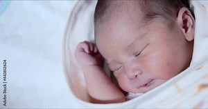 Asian newborn baby girl makes mouth movements extreme close-up shot. Adorable 0–6-month-old infant with closed eyes. Neonatal first days in life concept.