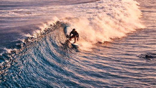 Surfers riding perfect waves under golden sunset light