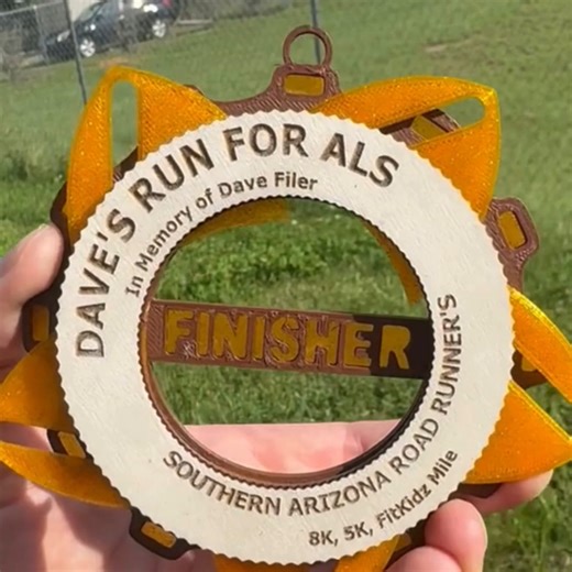 Dave's Run for ALS medal in action! This race features a unique finisher medal inspired by the Iris flower—it even opens and closes to reveal a surprise inside! You can earn this special medal in either the 8K or 5K. | Southern Arizona Roadrunners