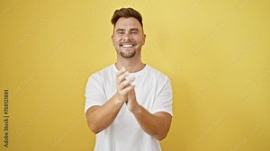Handsome young man clapping hands with a joyful expression against a yellow background
