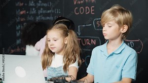 Smart girl using laptop programing engineering code with diverse friends ay table with microchip and main board scatter around in STEM classroom at blackboard written with coding prompt. Erudition. Stock Video