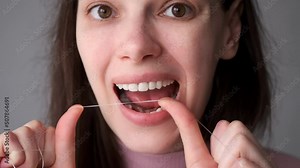 Portrait of young woman is cleaning her white teeth with dental floss smiling in bathroom. Everyday routine, hygiene of oral cavity at home. She is taking care about her teeth.