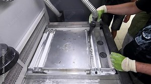 A male worker cleans the surface of an industrial 3D printer from white powder with a vacuum cleaner close-up. Multi Jet Fusion (MJF) 3D printing. The working process