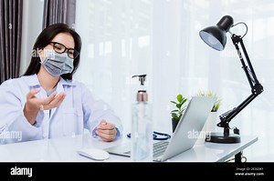 Asian young beautiful woman doctor wear face mask protective video call conference online raise hand explain to patients on laptop computer quarantine Stock Photo - Alamy