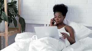 Happy attractive african american girl working office work remotely, Black woman using laptop computer and phone sitting in bed at home, Distance learning online education and work.