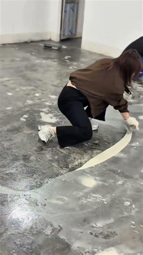 applying a thick layer of creamy white leveling compound to a concrete floor using a hand trowel