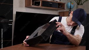 A male maintenance technician inspects a broken video set-top box at a client's home.