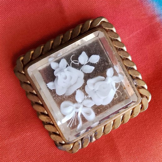 Antique lucite brooch, with engraved white flowers and a gilded brass frame.