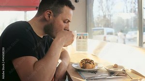 Young man eating croissant, drinking coffee in cafe in the city