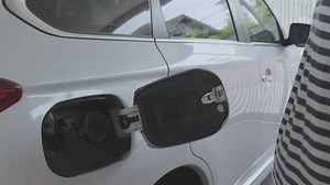 Woman charging her electric vehicle (EV) while using her mobile phone to control the process. It shows the convenience and efficiency of smart charging systems and integration of modern technology.