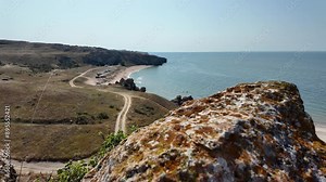 A panoramic view overlooking General's Beach in Crimea, Russia. The image shows a rocky cliff with a clear view of the coastline and the sparkling blue sea beyond.