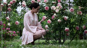 Young woman sitting and enjoying by blooming climbing pink rose in garden.