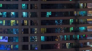 Rows of glowing windows with people in apartment building at night.