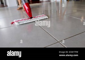 A red spray mop glides over a tiled floor, cleaning efficiently. Bright lighting highlights the mop's movement and water spray Stock Video Footage - Alamy
