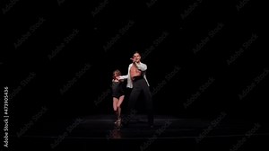 Young ballroom dancers couple on dark stage dancing Latin American program dance,hip rotations, steps,synchronous movements. Performance or competition preparation concept, ballroom dancing school ad.