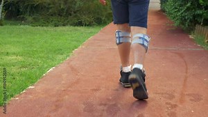 Slow motion steadicam shot of a kid walking outdoor with system of functional electrical stimulation. Treatment of foot drop with electrical signals stimulating the nerves in leg