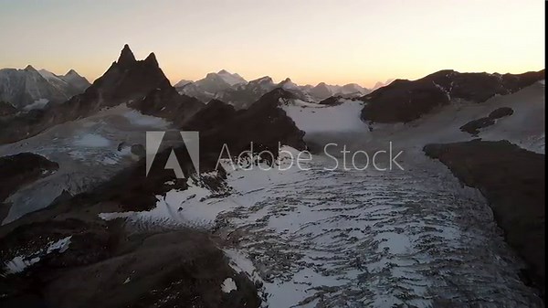 Aerial flyover over Glacier de Vouasson near Arolla in Valais, Switzerland at sunset with colorful glow behind the Aiguilles Rouges, Mont Blanc de Cheillon, Grand Combin and other peaks