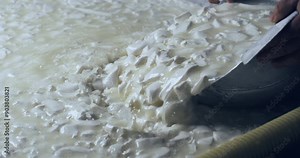 Super slow motion close up of artisan cheesemaker is mixing fresh bio eco milk mass during traditional cheese making process at cheese production creamery dairy factory at 1000 fps.