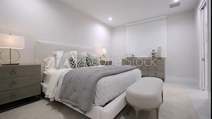 Stylish white walled bedroom interior design with multiple patterned pillows on bed and decorative table lamps on grey commodes