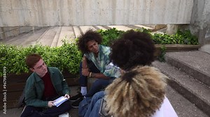 Diverse group of college students working on assignments outdoors, using notebooks and a tablet on campus. Multiracial Group of Students Studying Together on Campus Outdoors