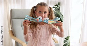 Beautiful cute girl with ponytails examines elegant iridescent blue shoes in her hands. Cute little fashionista. Happy child girl try on outfits
