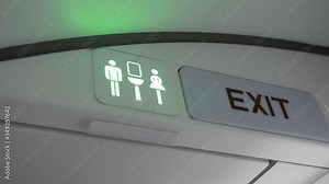 Airplane lavatory sign occupied to available. Shot of airplane lavatory sign turning from red (occupied) to green (available). Beside the lavatory sign is an exit sign.
