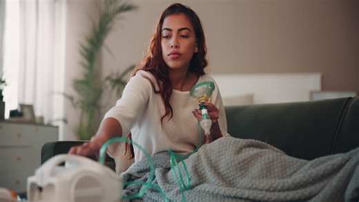 Woman sitting on a couch using a nebulizer for respiratory treatment | Premium Stock Video Footage