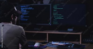 Cyber Terror - Computer Hacker sitting in a dark room in front of screens and writing lines of code while hacking