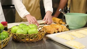 Close-up at hands of chef in cook uniform with apron, cooking class students stuff ingredients in pastry dough and pressing for bakery foods, prepare fruit pies in restaurant stainless steel kitchen.