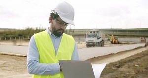 Male engineer in uniform and white helmet makes notes in notebook at work. Verification of works on the territory of the construction site. Industrial Building Construction Site. construction works .