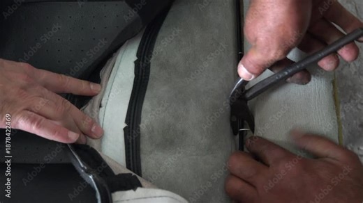 Hog ring attachment securing leather car seat cover during professional upholstery installation. Steel hog rings crimped with pliers provide durable long term fastening for automotive seating.