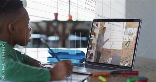 Boy writing homework at table, glancing at laptop while teacher starting lesson, charts overlaying
