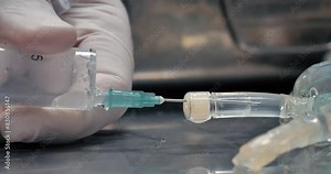 The doctor uses a syringe to draw a clear solution from a bottle for injection. Close-up of the process of drawing a solution into a syringe from a large bottle.