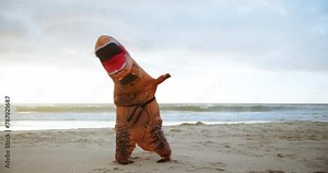 Beach, karate and adult in dinosaur costume on sand by ocean or sea for fitness and training. Exercise, health and workout by water with athlete person in t-rex outfit for discipline or self defense