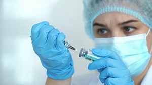 Close up of female doctor in medical gloves, white coat and protective mask fills syringe with drug. Nurse holds ampoule with vaccine for covid-19. Coronavirus