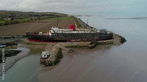 Derelict remains of liner ship docked on sandy coast, aerial orbit view