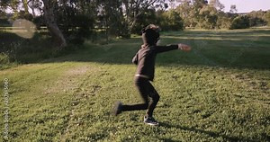 young boy wearing a homemade ninja mask and black costume practices ninja moves, karate, jumping, kicking and running around a park in the late afternoon golden glow of the setting sun