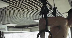 Training with gymnastic rings, strength exercise in closed gym. Men doing workout using rings