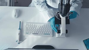 A dedicated scientist in a white lab coat operates a sophisticated microscope and keyboard, demonstrating expertise in researching and analyzing microsamples in a modern hightech lab