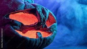 Halloween wrinkled pumpkin glowing inside in the dark. Scary carved pumpkin with smoke around it. Aged pumpkin glows on Halloween night. Close-up in 4K, UHD