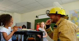 Young Caucasian male firefighter teaching schoolgirl about fire safety in classroom 4k