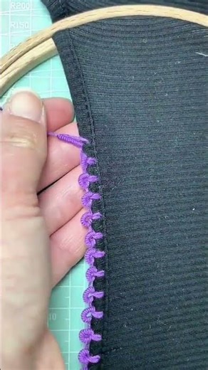 creating an intricate purple hand embroidery pattern along the edge of a dark fabric with a needle