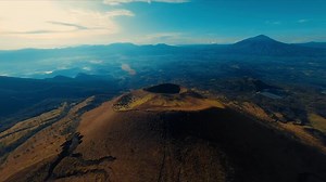 Aerial view of a volcanic landscape with a prominent crater and distant mountain under a clear sky.