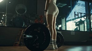 Young woman doing deadlift with heavy bar in gym, strong female athlete with muscular body lifting weights, exercising with barbell.