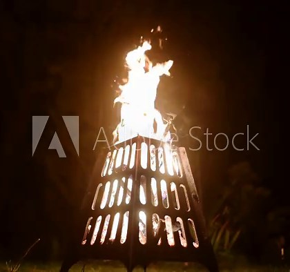 Bonfire with burning woods in the backyard at night. A convenient and safe bowl for an open fire. A metal portable fire pit is safe device for an outdoor picnic on the lawn or summer camp.