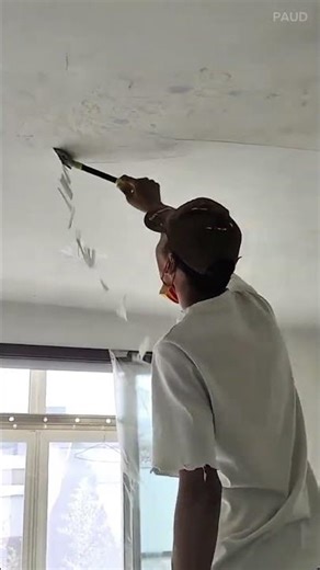 Scraping off old white paint from the indoor ceiling using a metal hand scraper tool for renovation