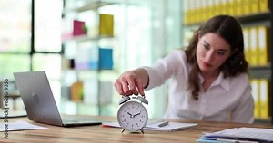 Business woman puts alarm clock on desktop in office. Time management concept overtime and deadline