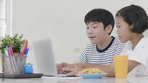 Young asian boy and girl playing with laptop computer at home. Children are playing online game on a laptop computer together. Dolly shot 60fps.