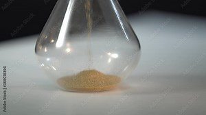 A pile of sand at the bottom of the hourglass, small grains of sand fall from above. Macro falling sand. Filance concept ot running time. Time is money.
