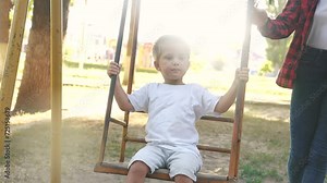 little boy swings on a swing. concept of a happy childhood and loving family. a child in white clothes swings on a swing on the playground, the boy is being filmed by his parents lifestyle